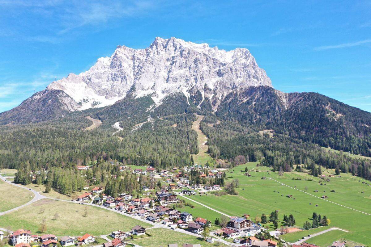 Beeindruckende Luftaufnahme eines majestätischen schneebedeckten Berges mit einem charmanten Dorf am Fuße und weiten Grünflächen.
