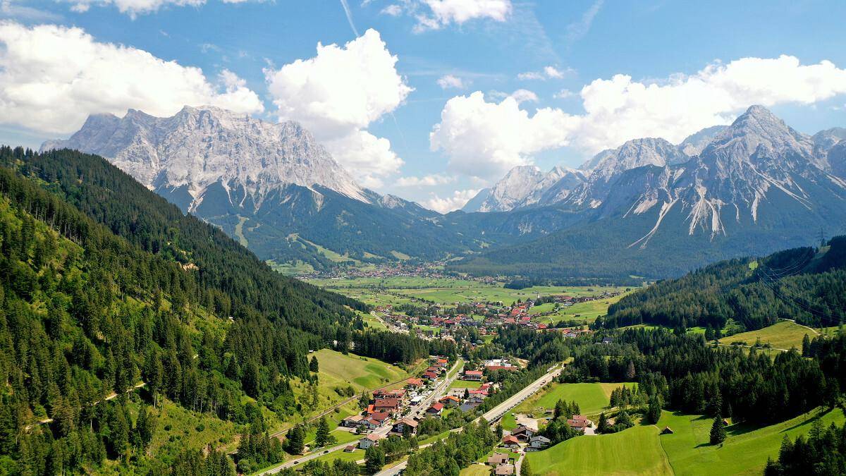 Weitläufiger Panoramablick auf ein malerisches Tal mit einem Dorf, umgeben von Bergen und Wäldern.