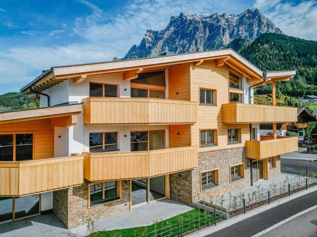 Neubau im alpinen Stil mit Holzverkleidung und Balkonen, umgeben von der beeindruckenden Berglandschaft.