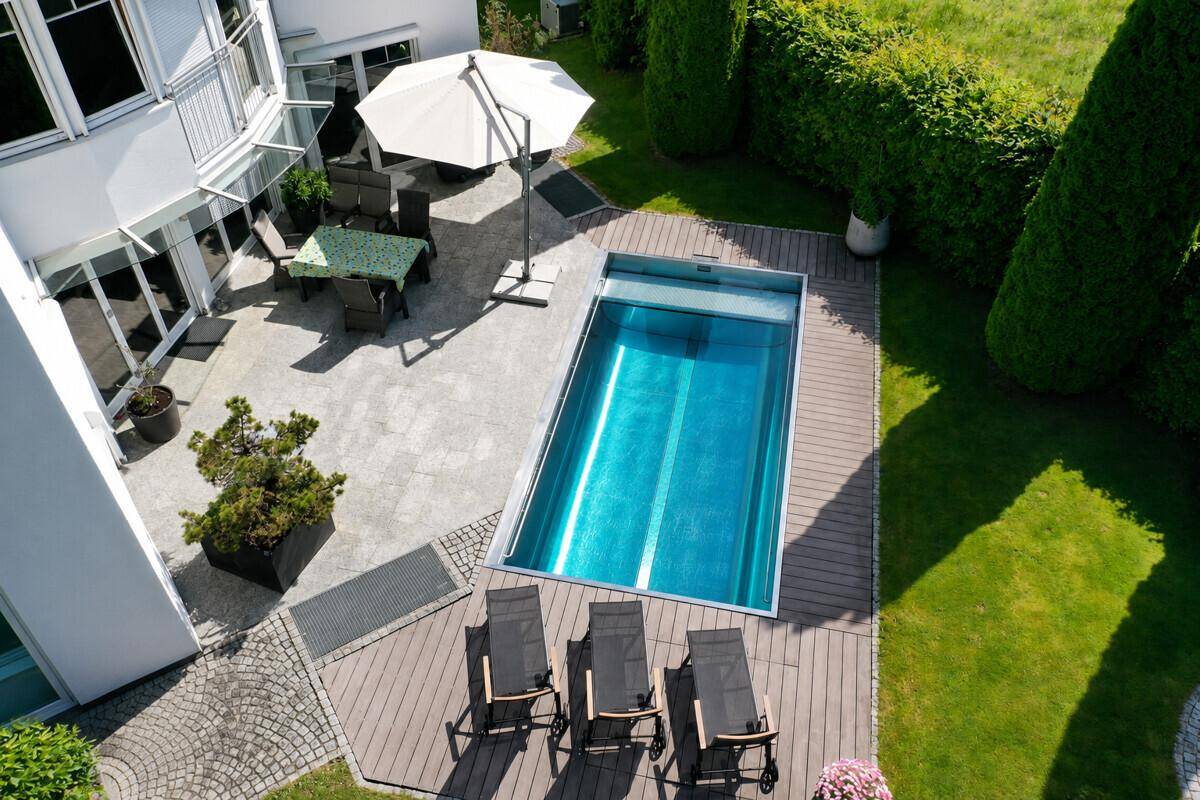 Vogelperspektive auf den Garten mit Pool, Holzdeck, Liegestühlen und einer gepflasterten Terrasse.