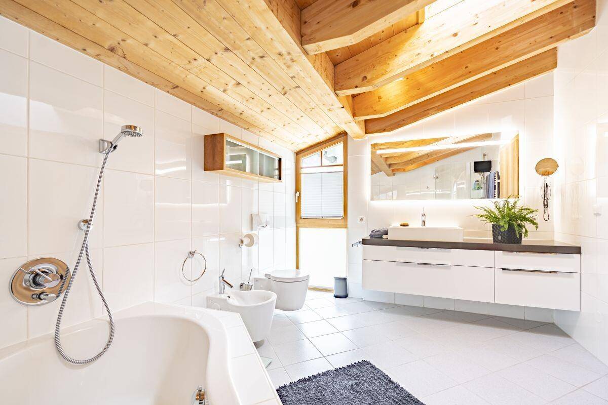 Modernes Badezimmer mit Holzbalkendecke, Badewanne, Bidet und Doppelwaschbecken.
