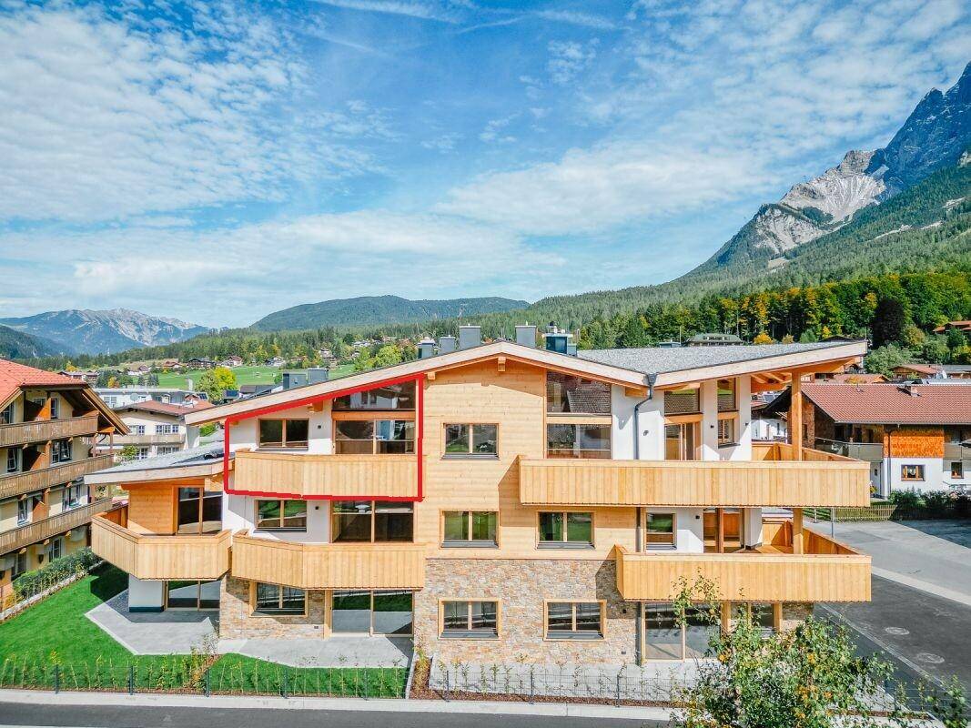 Moderne Alpenarchitektur mit Holzfassade und Balkonen, umgeben von einer beeindruckenden Berglandschaft.