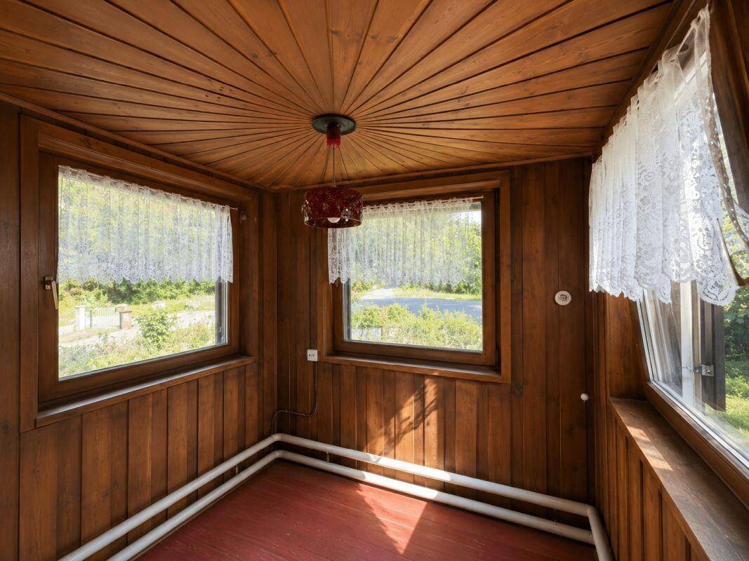 Gemütlicher Wintergarten mit Holztäfelung an Wänden und Decke, bietet viel Licht und Ausblick.