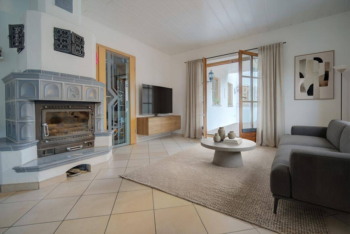 Wohnzimmer mit Kachelofen, Fliesenboden und Zugang zu einem Außenbereich.