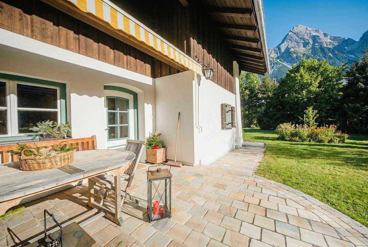 Gemütliche Terrasse mit Holztisch, Markise und herrlichem Bergblick, umgeben von Grünflächen.