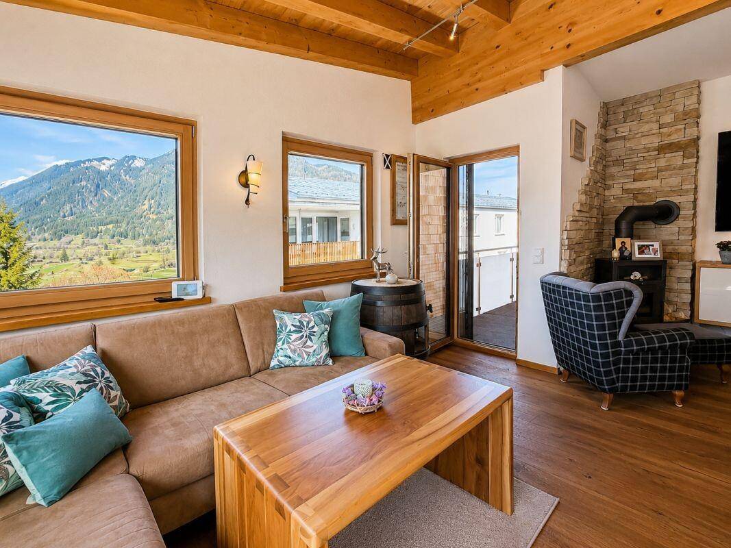 Gemütliches Wohnzimmer mit Sofa, Holzkamin und Bergblick durch große Fenster.
