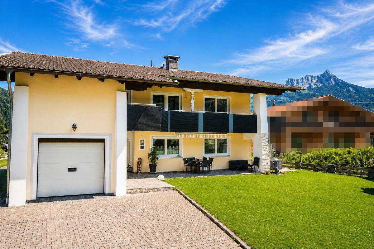 Vorderansicht des Hauses mit Garage, gepflasterter Auffahrt und Terrasse mit Bergblick.