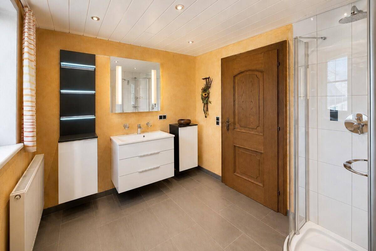 Modernisiertes Badezimmer mit Dusche, Waschtisch und grauen Fliesen an Wänden und Boden.