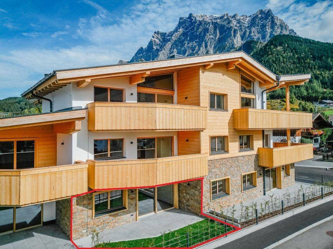 Ansicht des modernen Gebäudes mit Holzverkleidung und einer markierten Erdgeschossterrasse mit Gartenanteil.