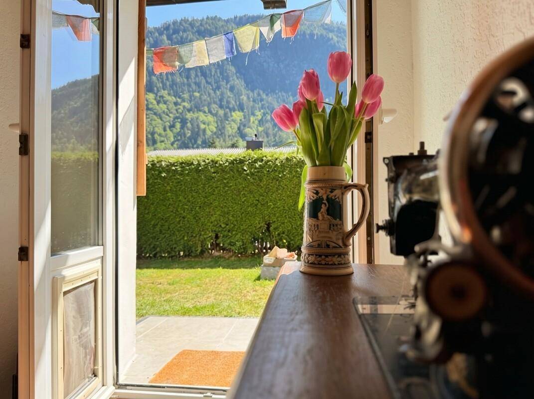 Offene Tür zum Garten mit Blick auf die umliegende Berglandschaft und bunte Gebetsfahnen.