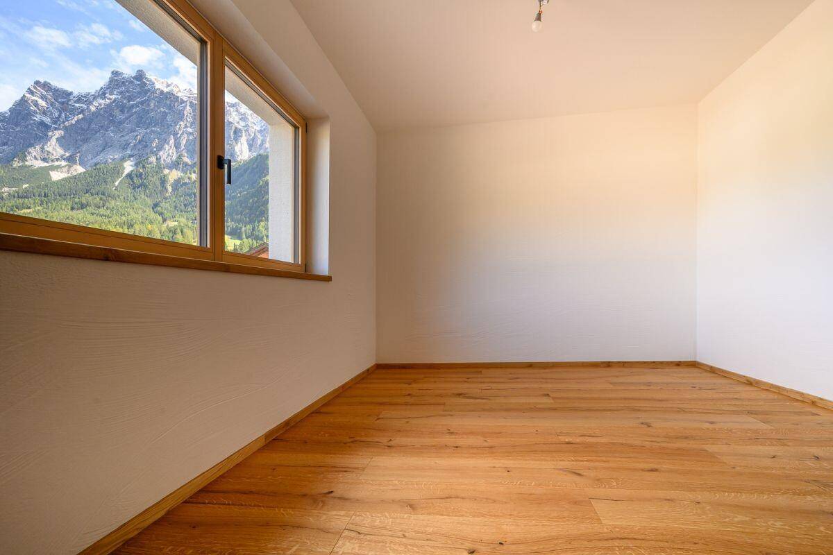 Helles Zimmer mit Holzboden und großem Fenster, das einen weiten Bergblick bietet.