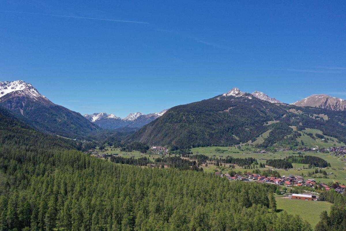 Panoramablick über ein weites Tal mit Dörfern, Wäldern und majestätischen Bergen im Hintergrund.