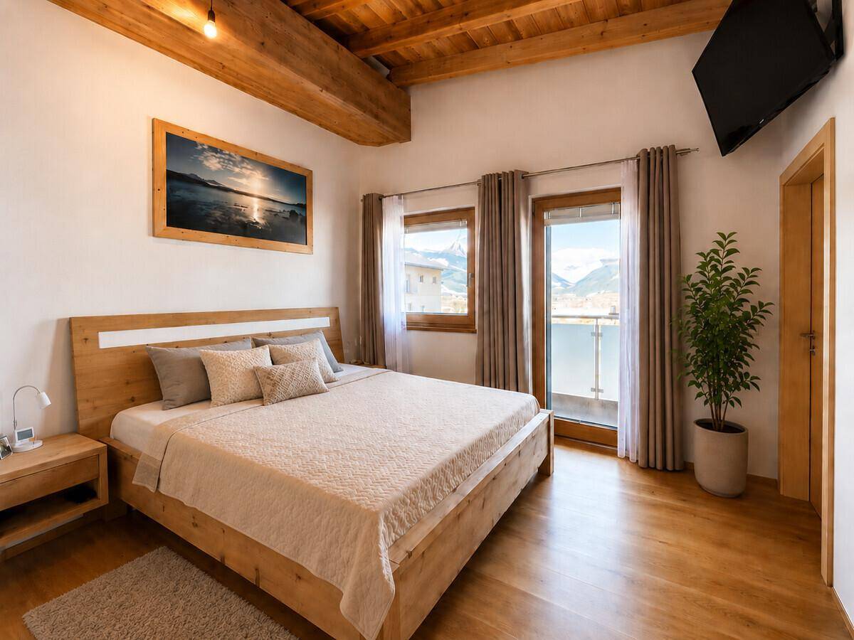 Helles Schlafzimmer mit Holzbett, Holzbalkendecke und Balkonzugang mit Bergblick.