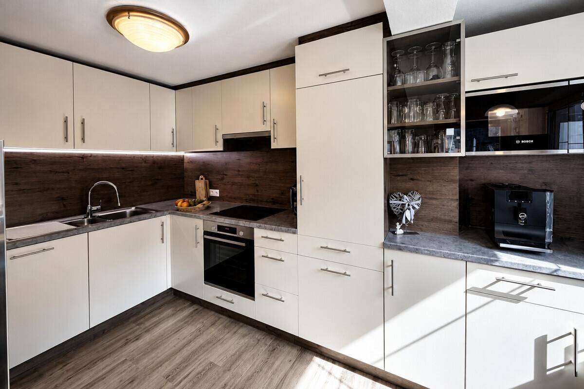 Moderne Einbauküche mit weißen Schränken, dunkler Holzrückwand und integrierten Geräten.