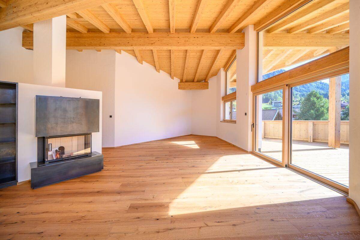 Heller, leerer Wohn-Essbereich mit Holzbalkendecke, Kamin und Zugang zur Terrasse.