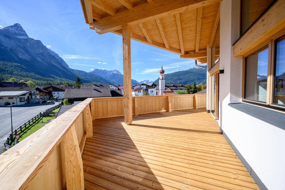 Sonniger Holzbalkon mit weitem Blick auf die Berge und ein Dorf mit Kirchturm.