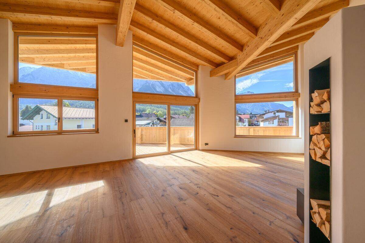Lichtdurchfluteter Wohnraum mit Holzbalkendecke, Bergblick und Zugang zu einem Außenbereich.