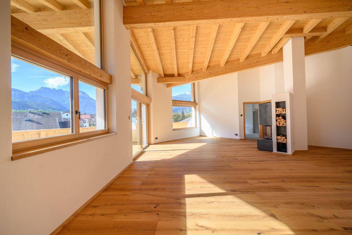 Geräumiger Wohnbereich mit Holzboden, großen Fenstern und Bergblick, bereit zur Einrichtung.
