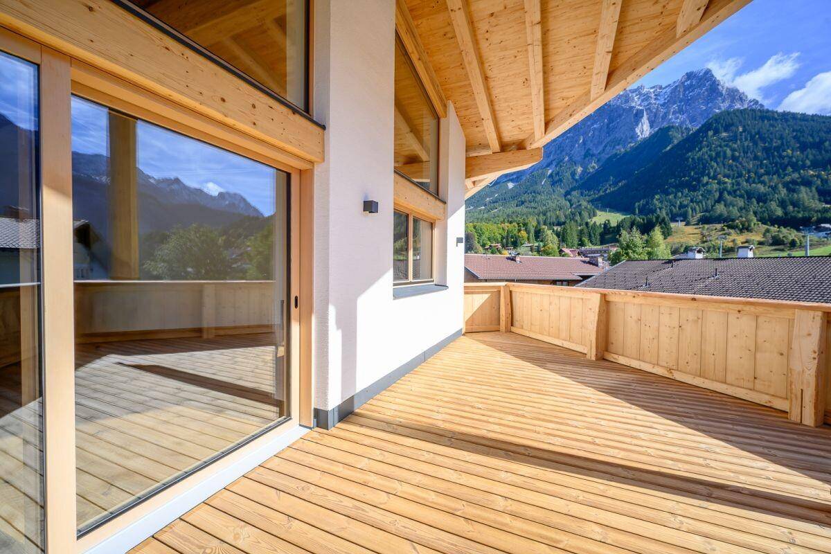 Geräumige Holzterrasse mit Bergblick und großen Glasschiebetüren zum Innenbereich.