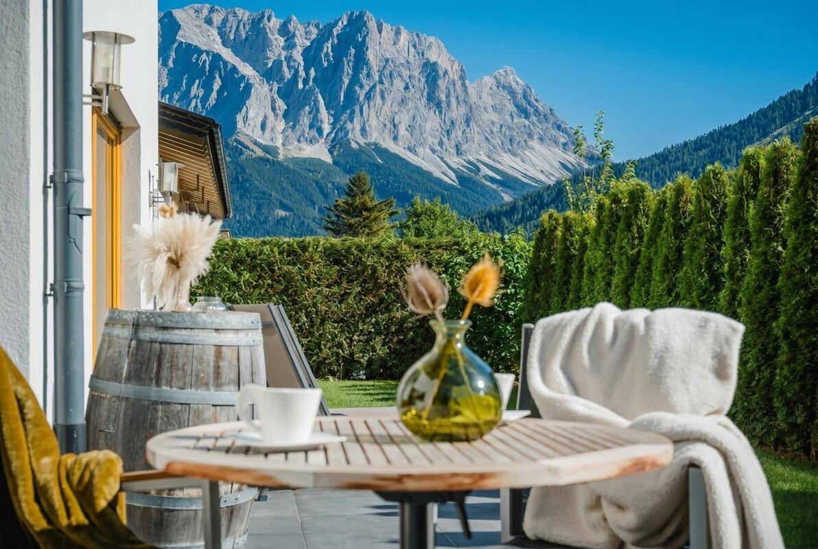 Gemütlicher Terrassenbereich mit Holztisch, Decke und atemberaubendem Bergblick im Sonnenschein.