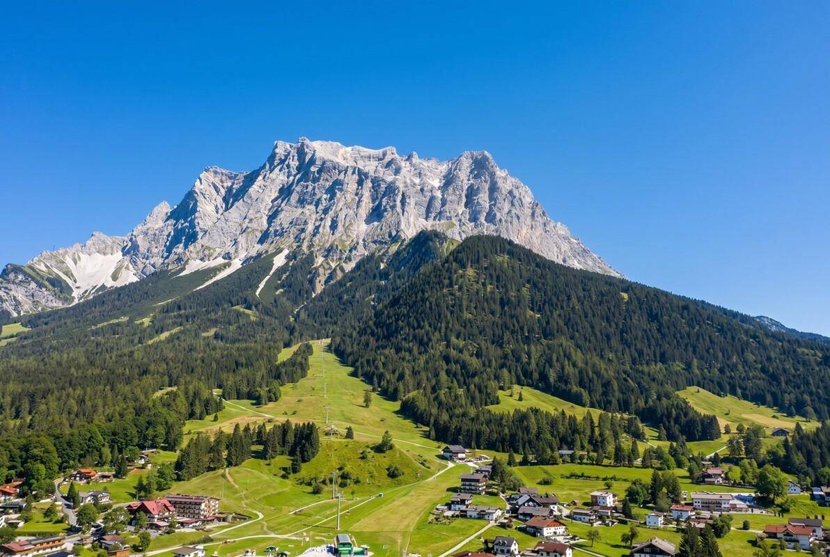 Beeindruckende Luftaufnahme eines großen Bergmassivs mit Skipiste und umliegendem Dorf.
