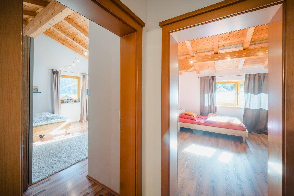 Blick in zwei helle Schlafzimmer mit Holzbalkendecken und gemütlicher Atmosphäre.