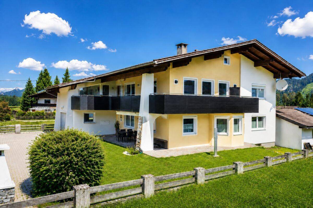 Charmantes Haus mit sonniger Terrasse, Balkonen und weitläufigem Gartenbereich vor Bergpanorama.