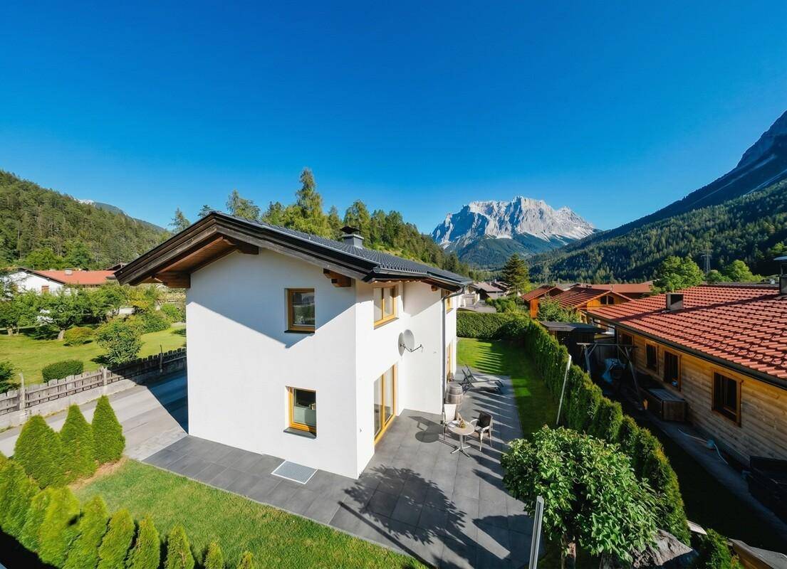 Ansicht des Hauses von oben mit Terrasse, Garten und beeindruckendem Bergpanorama.