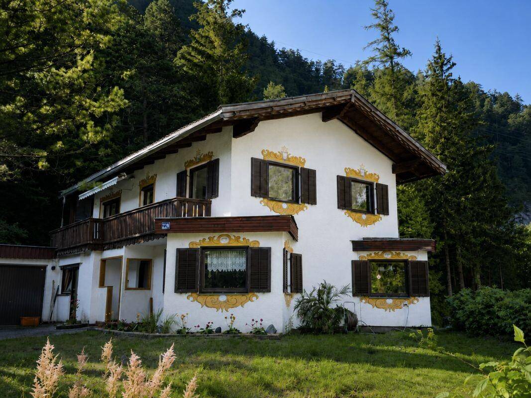 Charmantes Haus mit traditioneller Architektur und Holzbalkon, eingebettet in eine grüne Landschaft mit Bäumen.