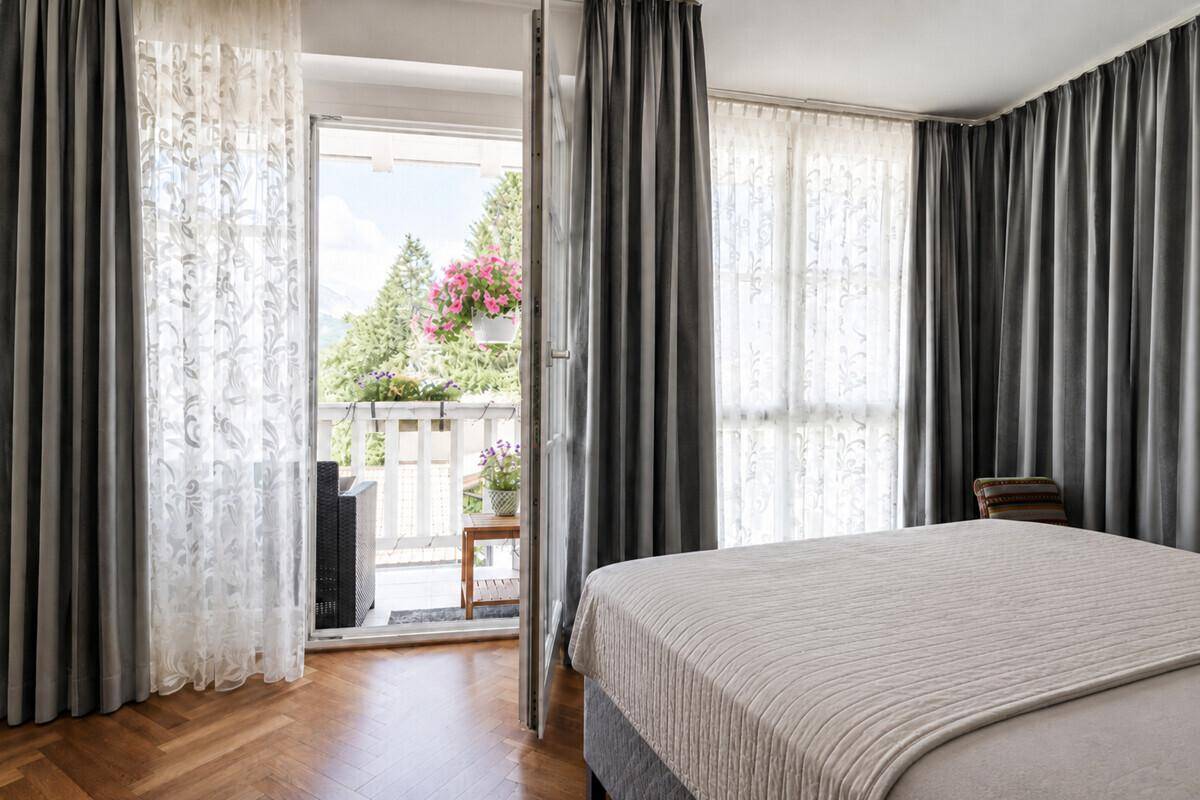 Schlafzimmer mit Zugang zu einem Balkon, Holzboden und viel Tageslicht durch große Fenster.