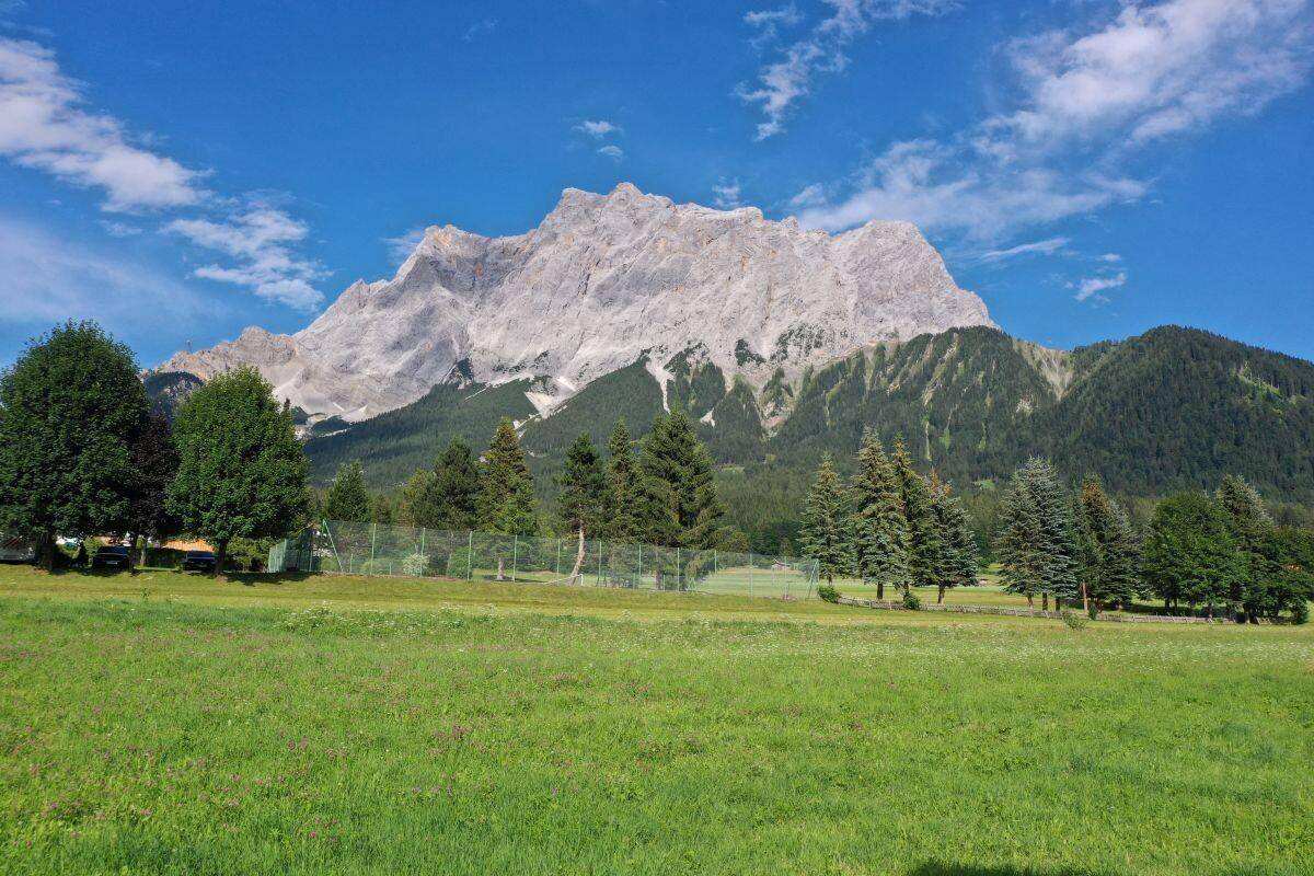Malerische Berglandschaft mit weiten grünen Wiesen und einem Tennisplatz im Vordergrund unter strahlend blauem Himmel.