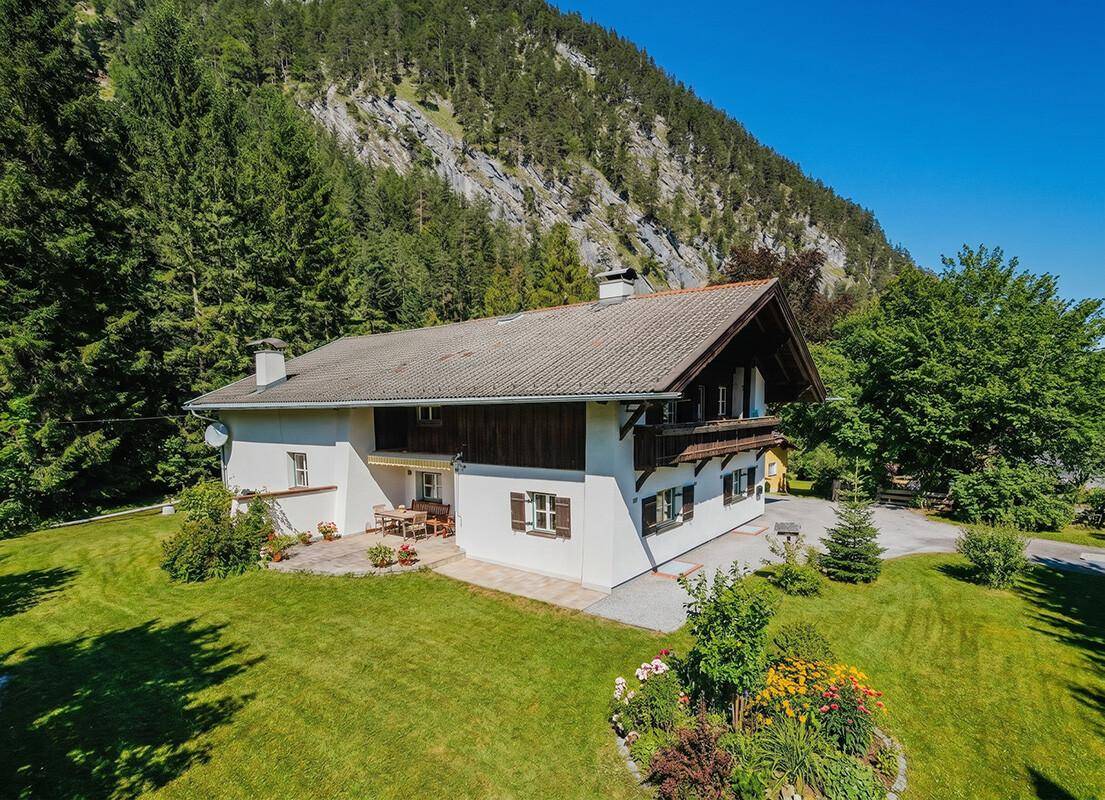 Luftaufnahme des Hauses mit großem Garten, umgeben von Wald und beeindruckender Bergkulisse.