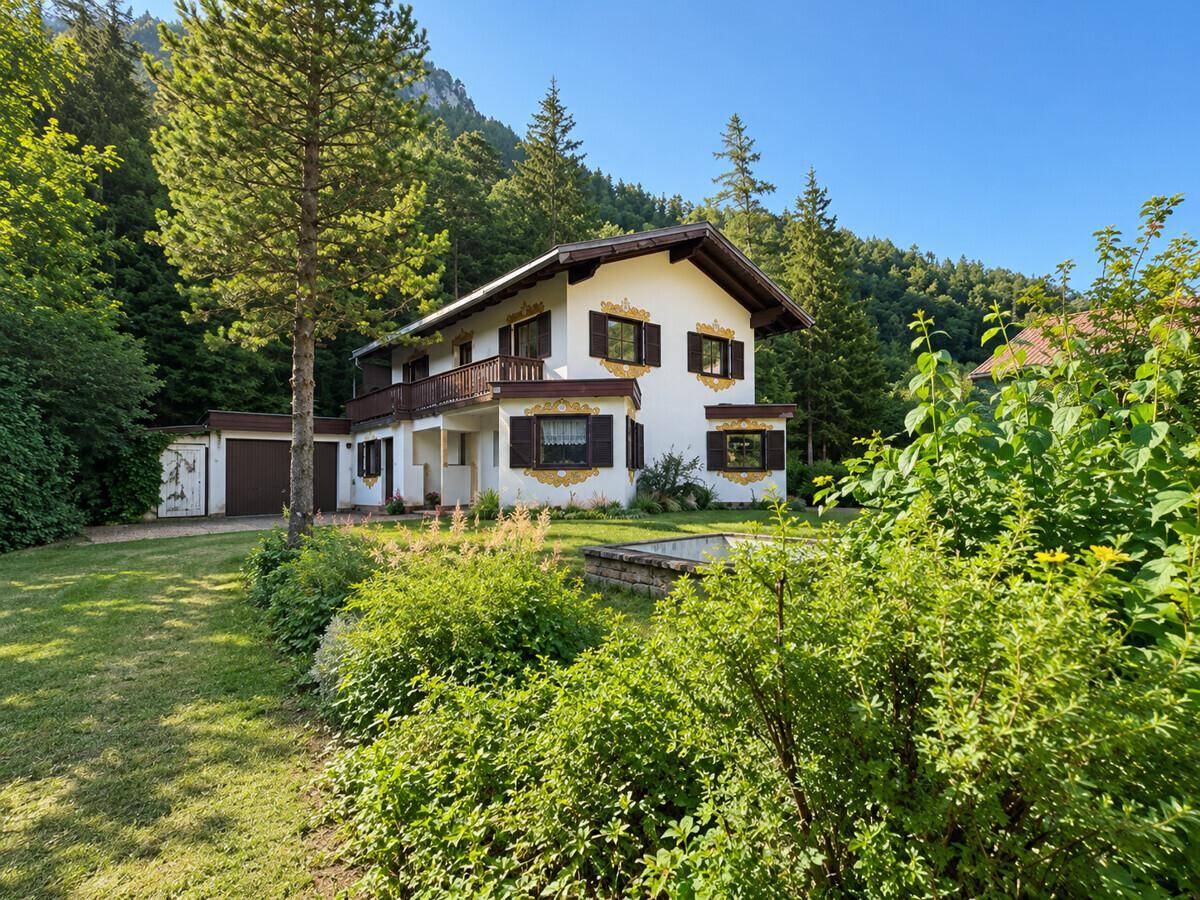 Charmantes Haus mit traditioneller Architektur, umgeben von einem gepflegten Garten und hohen Bäumen.