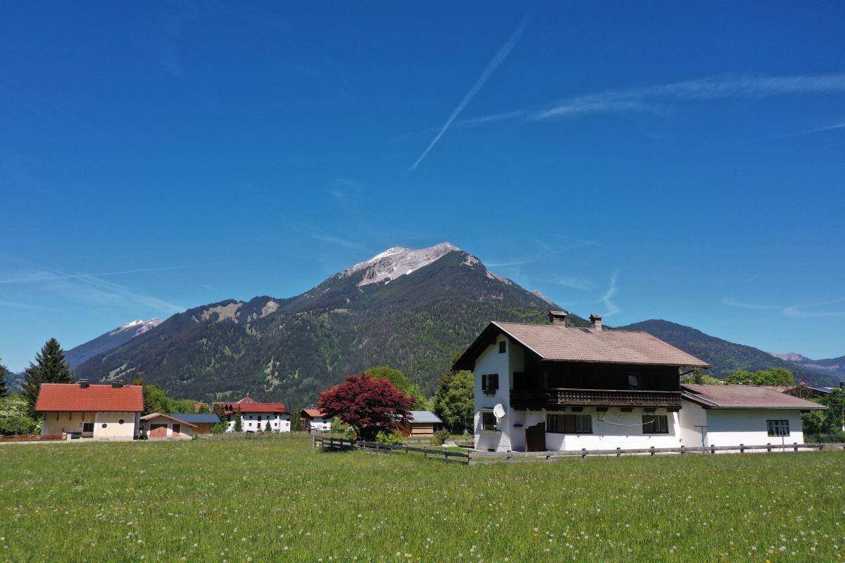 Traditionelles Haus in ländlicher Umgebung mit weiten Wiesen und majestätischem Bergpanorama.