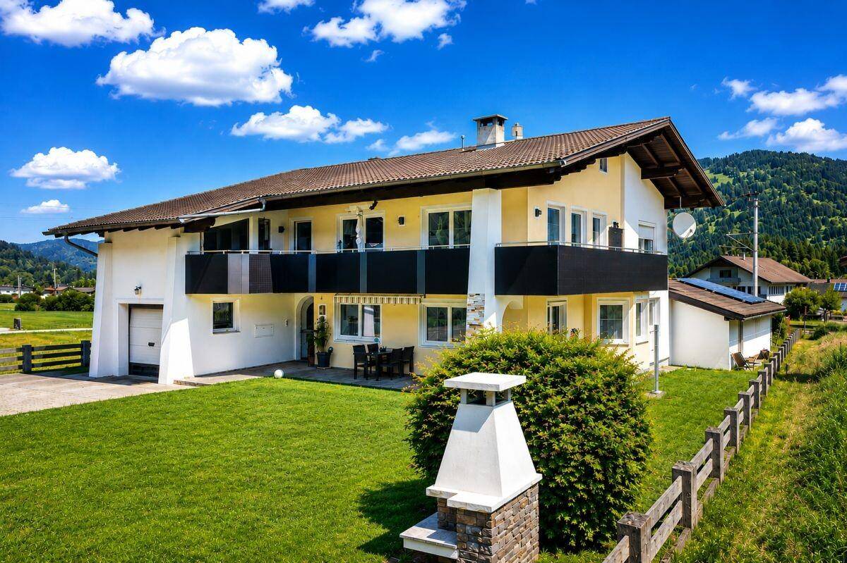 Attraktives Wohnhaus mit Balkonen, gepflegtem Rasen und schöner Bergkulisse im Hintergrund.