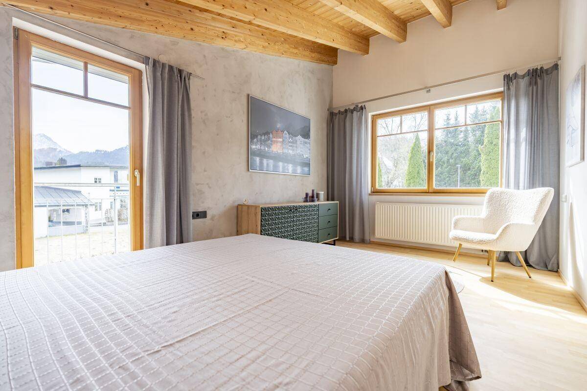 Gemütliches Schlafzimmer mit Holzboden, großem Fenster und Zugang zu einem Balkon.