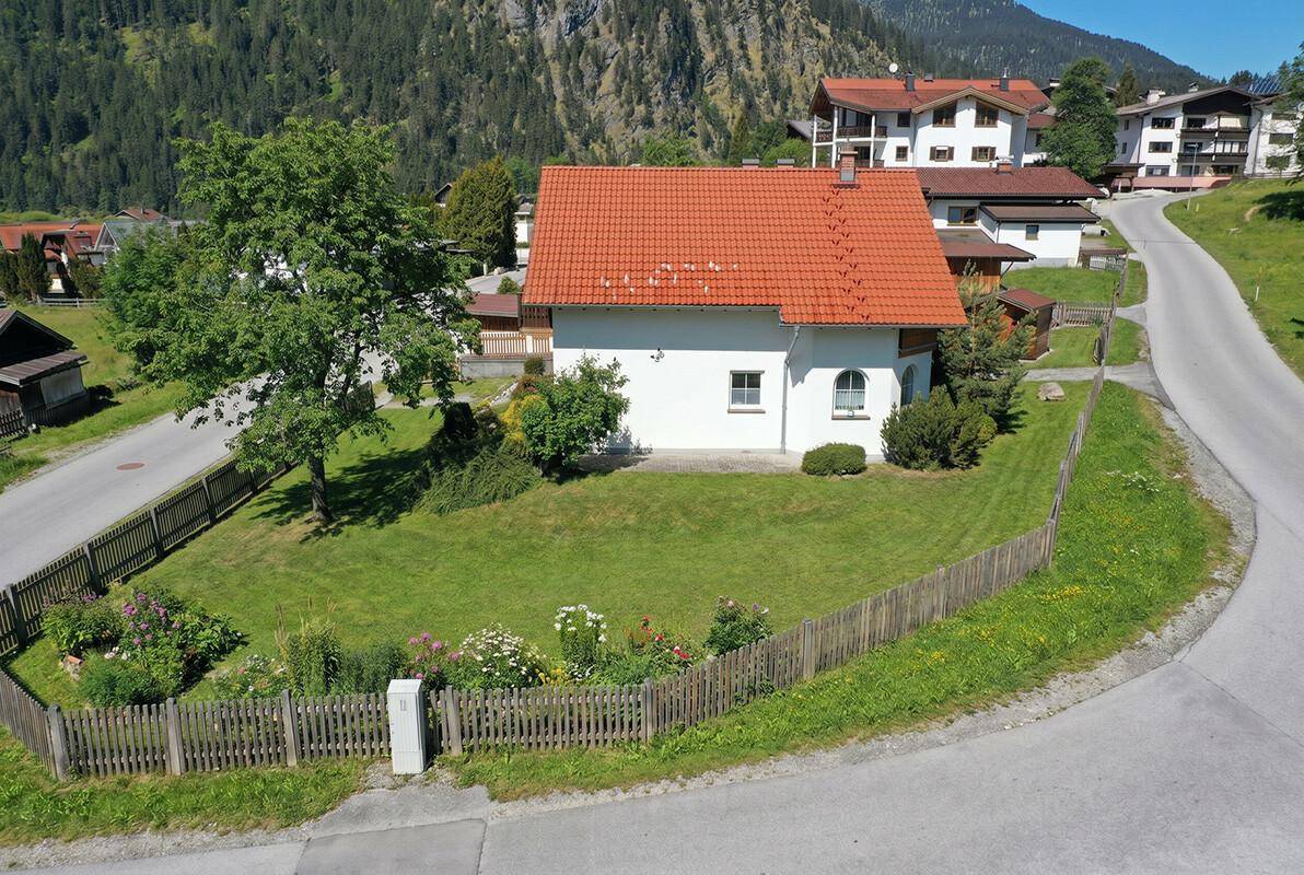 Gepflegter Gartenbereich mit Rasenfläche und Blumenbeeten vor einem traditionellen Haus.