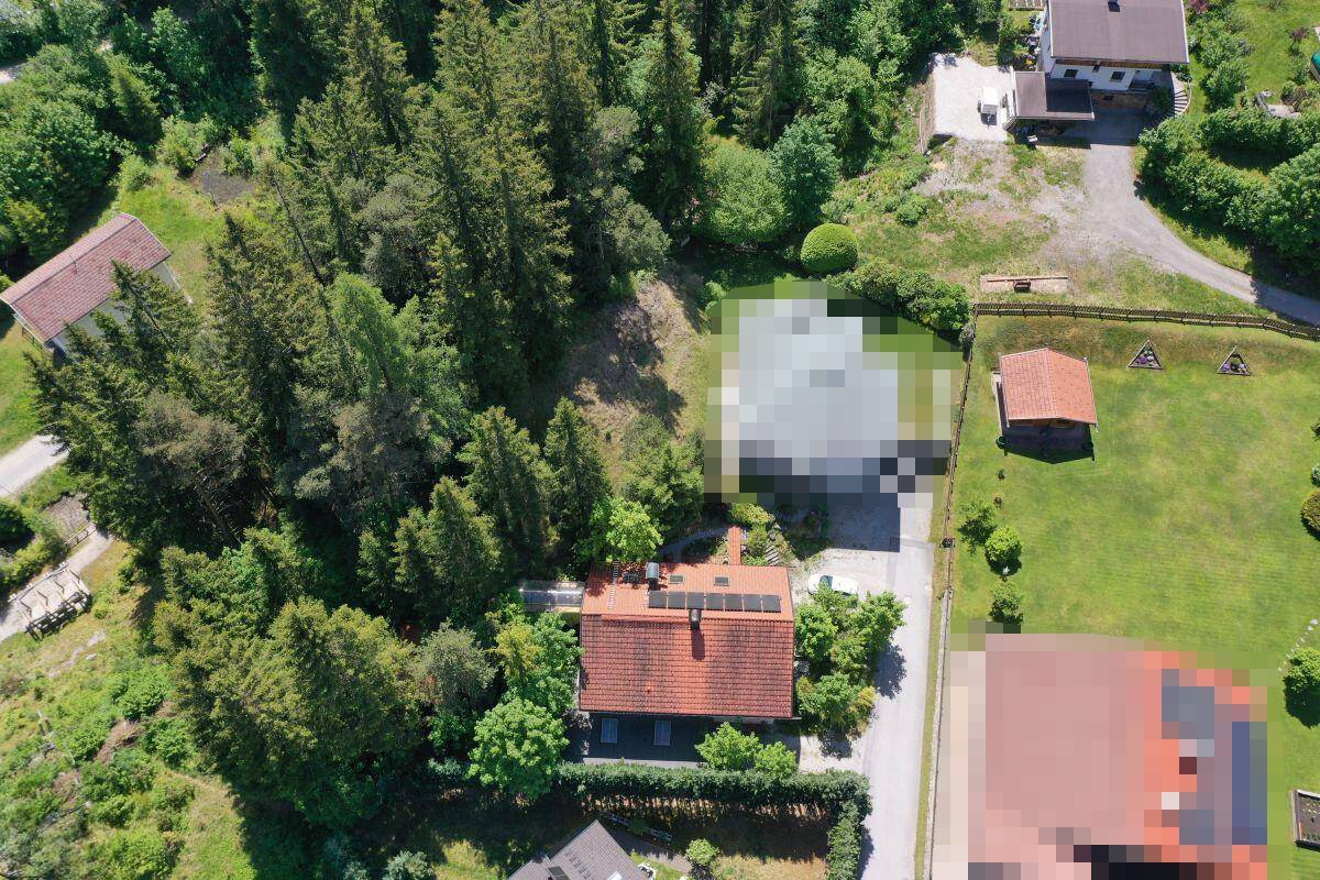 Weitläufige Luftaufnahme des Anwesens mit Wald, Wiesen und umliegenden Häusern in den Bergen.