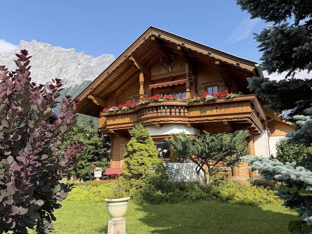 Charmantes Holzchalet mit blühenden Blumenkästen und majestätischer Bergkulisse im Hintergrund.