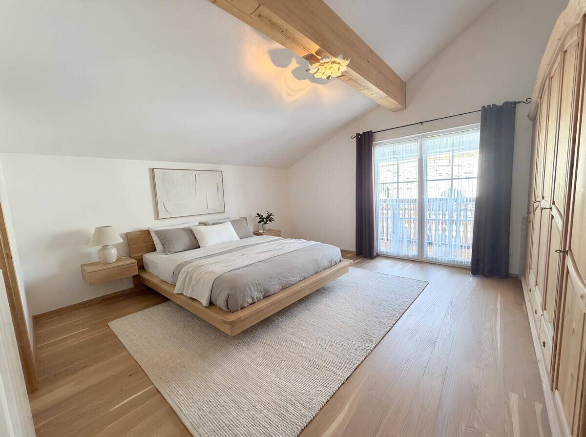 Helles Schlafzimmer mit Holzbalken, Parkettboden und Zugang zu einem Balkon.