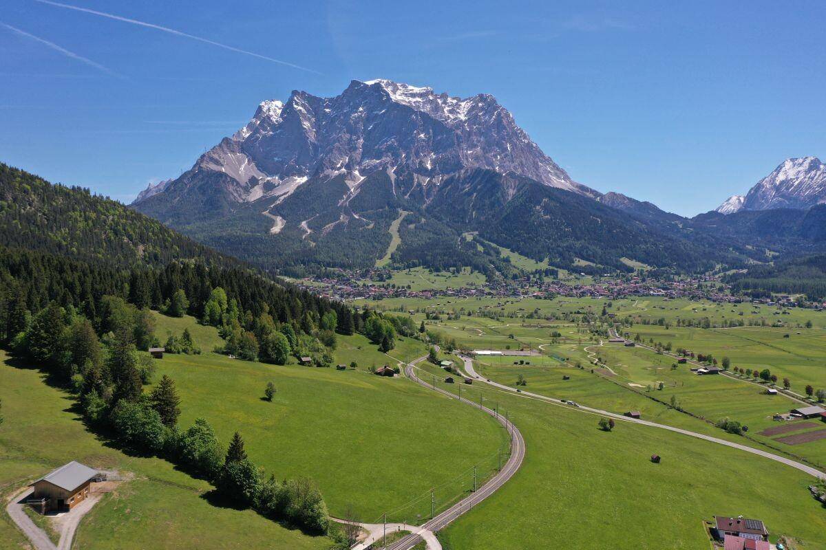 Weitläufige Luftaufnahme einer alpinen Landschaft mit einem Dorf, Feldern und einem majestätischen Berg.