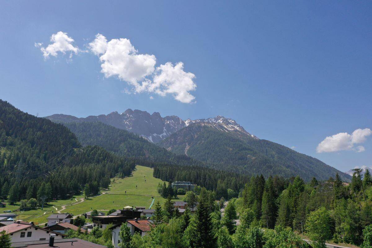 Panoramablick auf die majestätische Berglandschaft mit grünen Wäldern und einem Skihang.