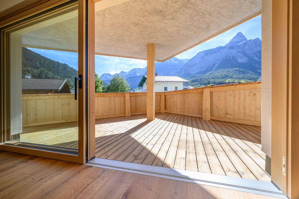 Geräumige, unmöblierte Terrasse mit Holzboden und beeindruckendem Bergblick unter blauem Himmel.