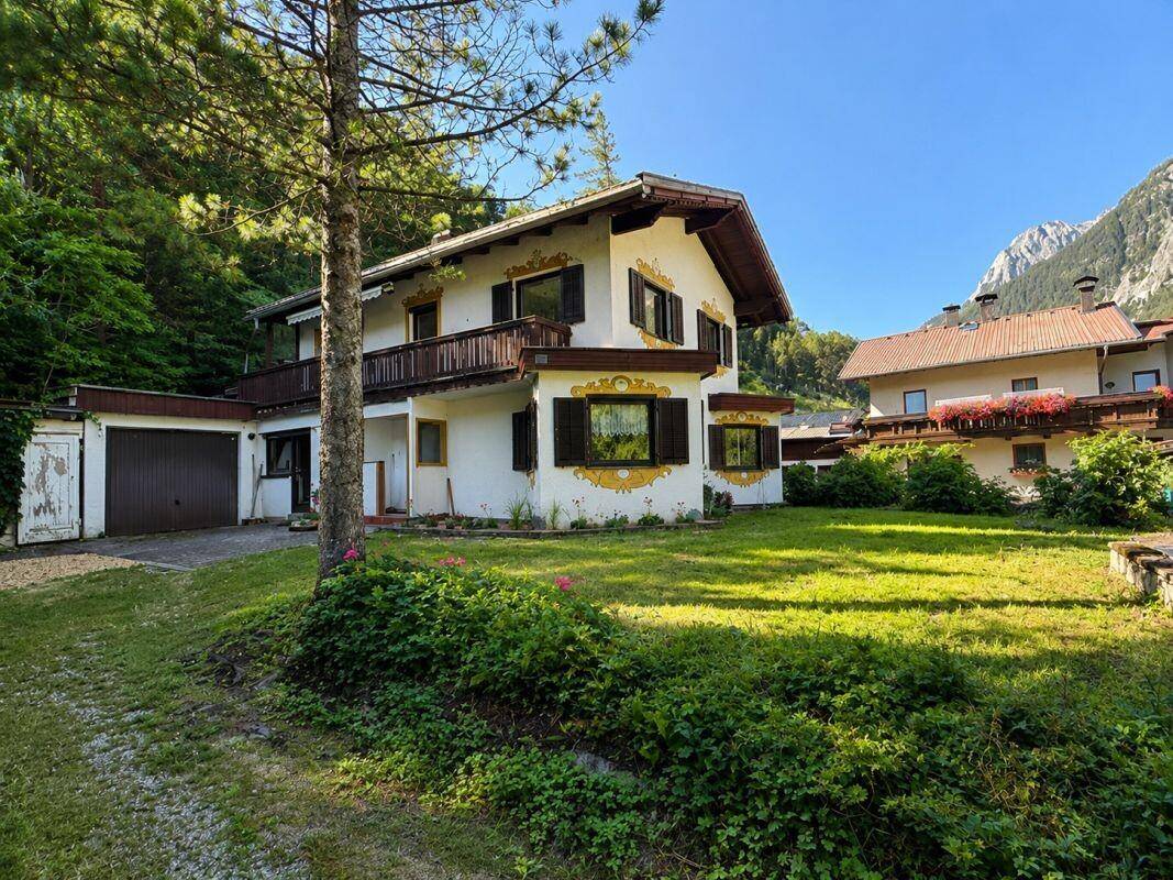 Traditionelles Haus mit bayerischer Fassade und Garage, umgeben von einem gepflegten Garten mit Bergblick.