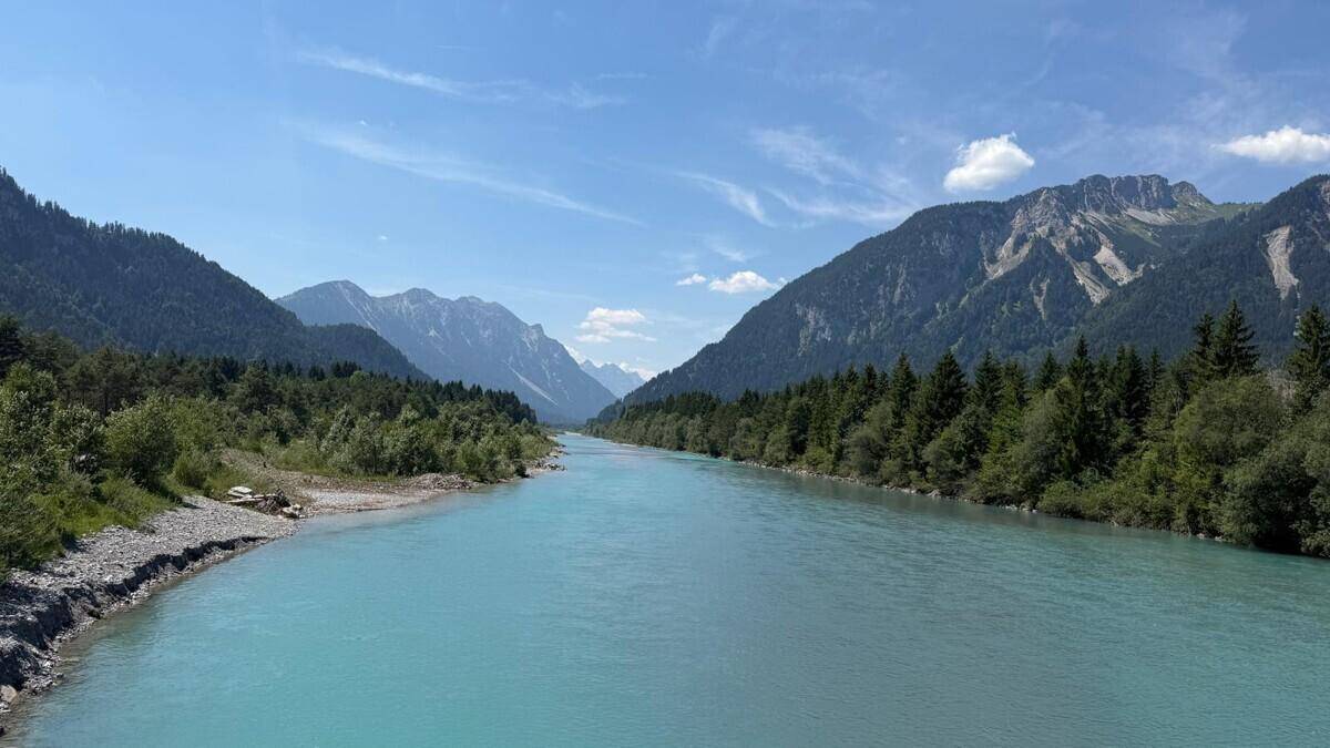 Panoramablick auf ein weites Flusstal mit klarem Wasser und bewaldeten Bergen.