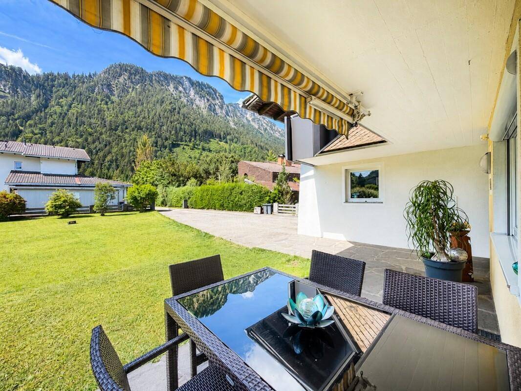 Überdachte Terrasse mit Markise, Gartenmöbeln und Blick auf die Berge.
