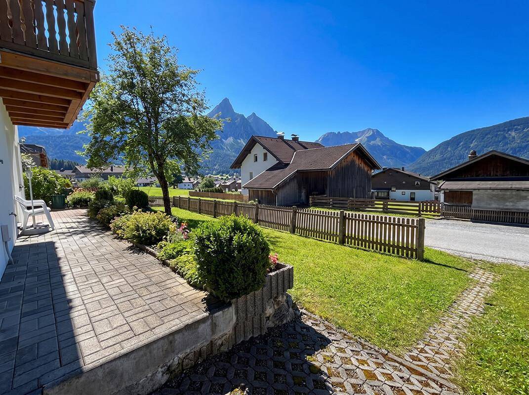 Seitlicher Gartenbereich mit gepflastertem Weg und Blick auf die alpine Bergwelt.