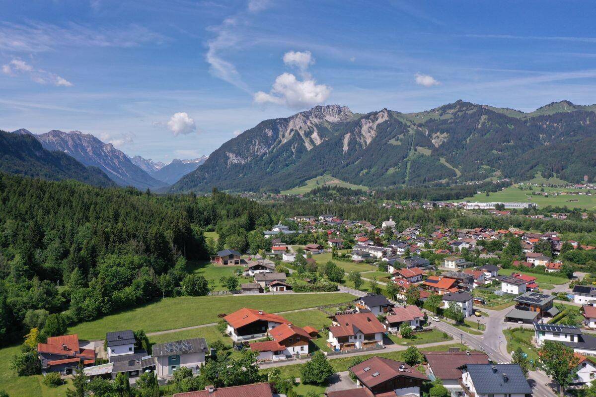 Panoramablick aus der Vogelperspektive auf eine ländliche Gemeinde, eingebettet in eine grüne Landschaft mit hohen Bergen.