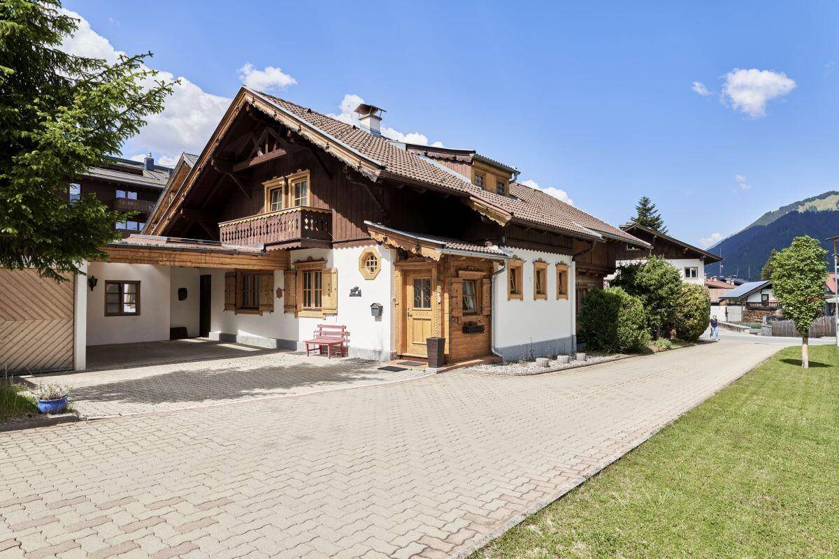 Traditionelles Haus mit Holzdetails, gepflasterter Auffahrt und Carport in alpiner Umgebung.