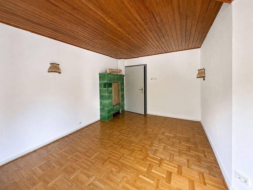 Geräumiges Wohnzimmer mit Holztäfelung an der Decke und einem traditionellen grünen Kachelofen.